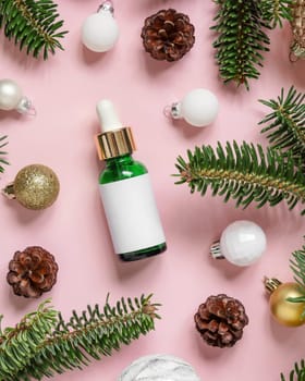 Green Dropper Bottle near Christmas decorations, fir branches and pine cones on pink top view. Holiday brand packaging mockup. Skincare beauty product, cream or serum. Healthcare natural cosmetics