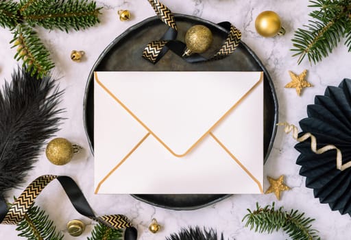 Black and golden Table setting with ornaments and fir tree branches top view, envelope mockup. Christmas or New Year atmospheric composition on marble table, copy space.
