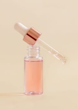 Opened Bottle with serum drop falling from pipette cap on light beige, close up, copy space. Skincare cosmetic product, essence or serum. Everyday beauty routine.