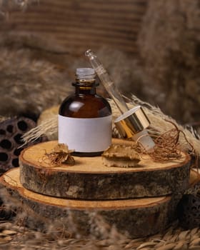 Opened glass bottle on wood near natural boho decorations close up, cosmetics label mockup. Eco friendly Skincare beauty product, serum or essence. Bohemian composition with dried leaves and flowers.