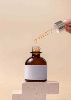 Hand holding pipette with drop falling down into opened dropper bottle on stones on light beige, close up, cosmetic label mockup. Natural skincare product, serum or essential oil.