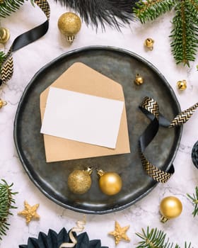 Black and golden Table setting with ornaments and fir tree branches top view, invitation card mockup. Christmas or New Year atmospheric composition on marble table, copy space.
