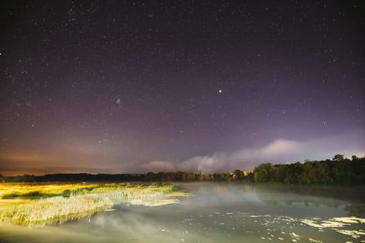Evaporation Over River Lake At Night. Milky Way Galaxy In Night Starry Sky Above Lake River Landscape At Night. Glowing Stars Above Summer Nature.