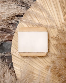 Handmade soap bar with blank label on dried palm leaf near pampas grass top view, mockup. Skincare beauty product. Bohemian eco friendly cosmetics flat lay with dried leaves.