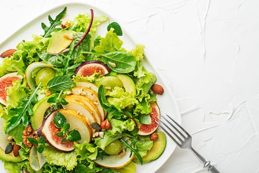 Fresh green leafy salad with fruits and nuts on white background close up. Concept for a tasty and healthy meal