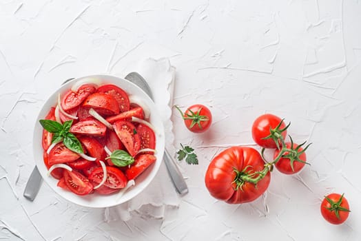 Fresh tomato salad with onion and basil on white table background. Concept for a tasty and healthy meal