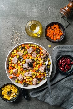 Healthy mixed tuna salad with corns, carrots, peas, beans and olives on grey table background. Mexican corn salad.