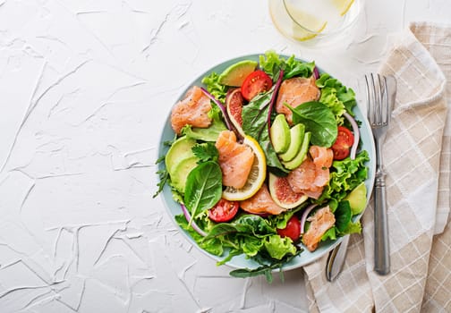 Fresh green salad with smoked salmon, cherry tomatoes, fig and avocado on white table background
