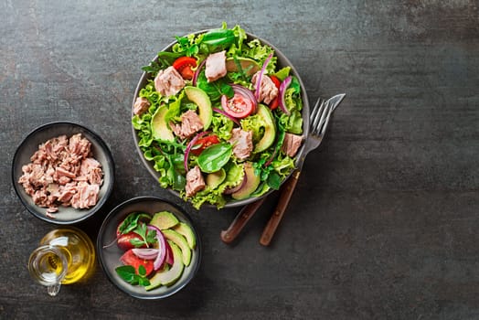 Fresh green leafy salad with tuna avocado and tomato on grey table background. Concept for a tasty and healthy meal