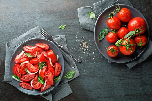 Fresh tomato salad with onion and herbs on a grey table background. Concept for a tasty and healthy meal