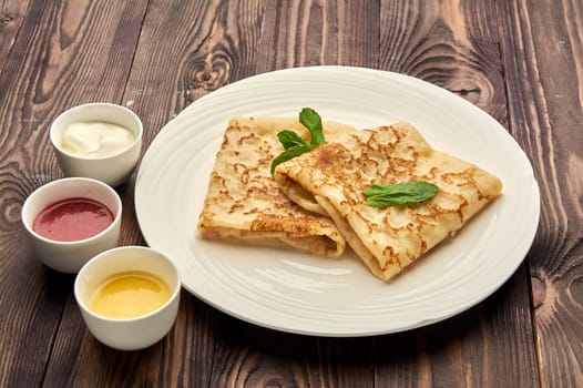 delicious juicy pancakes lie on a white plate with sauces standing next to them. High quality photo