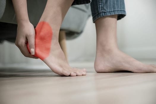 Asian young woman sitting on sofa holding her feet and stretch muscles have symptoms feeling pain, beautiful female problems with foot at home, painful ankle injury, Health care and medical concept