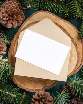 Horizontal blank card and envelope between fir branches and pine cones on green close up, mockup. Christmas or New Year greeting card template, Holiday winter composition