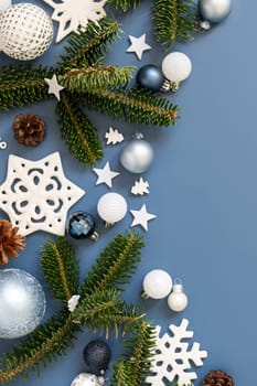 White Christmas decorations and fir tree branches on a blue top view with copy space. New Year and Christmas holiday atmospheric flat lay with baubles, snowflakes and stars