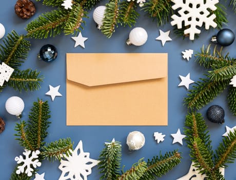 Craft paper envelope on a blue background near white Christmas decorations and fir branches top view, mockup, copy space.. New Year and Christmas holiday atmospheric flat lay