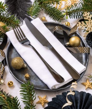 Black and golden Christmas table setting with decorations and fir tree branches close up. Winter table with fork, knife and plate. Winter New Year or Christmas dinner atmosphere