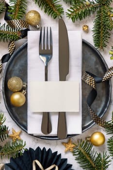 Black and golden Table setting with ornaments and fir tree branches top view, place card mockup. Christmas or New Year atmospheric composition flat lay, copy space.