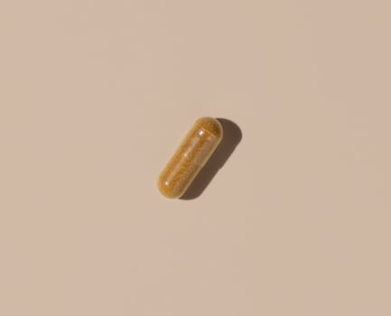 Brown medical capsule on light beige top view, hard shadows. Preventive medicine and healthcare, taking dietary supplements and vitamins. Minimal composition