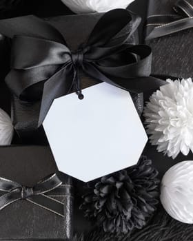 Gift Boxes with Black and white paper flowers and decorations, square gift tag Mockup, copy space. Dark composition with blank label card for Christmas, New Year, Birthday, Anniversary
