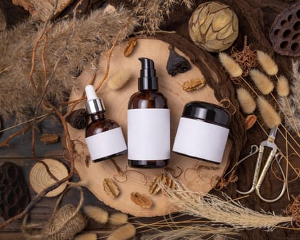 Refillable glass bottles on wood near natural boho decorations top view, label mockup. Skincare beauty product, lotion or essence. Bohemian eco friendly cosmetics flat lay with dried leaves.