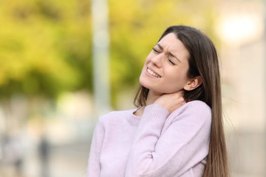 Teen complaining due neck ache standing in a park
