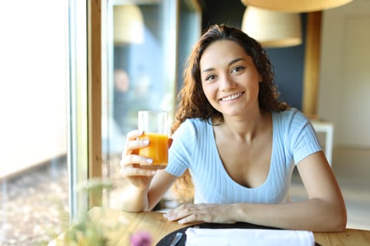 Woman holding orange juice glass looking at camera in a restaurant