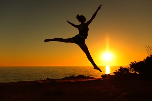 Side view backlight silhouette of a ballerina dancing ballet at sunset on the beach