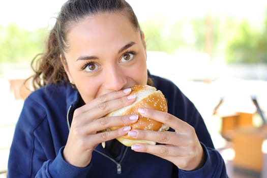 Front view portrait of a woman eating a burger looking at camera