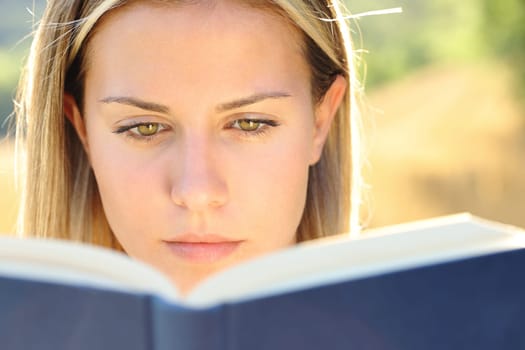 Front view close up portrait of a young woman reading a paper book in nature