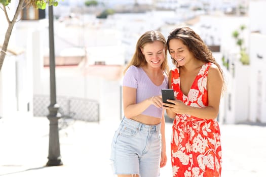 Happy tourists in a white town street checking smart phone on summer vacation
