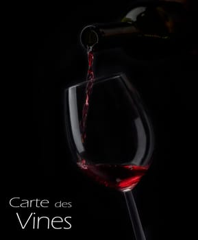 Red wine pouring in wineglass from bottle over black background. Wine list design menu with copyspace. Alcohol beverage card backdrop.