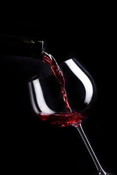 Red wine pouring in wineglass from bottle over black background. Wine list design menu with copyspace. Alcohol beverage card backdrop.