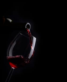 Red wine pouring in wineglass from bottle over black background. Wine list design menu with copyspace. Alcohol beverage card backdrop.