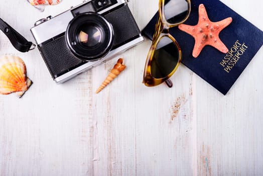 Vintage photo camera, passport, sunglasses and seashells border on wooden white background. Summer holiday design with copyspace. Traveling concept.