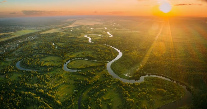 Aerial View. Beautiful Sunset Sun Sunshine Above Green Forest, Meadow And River Landscape In Sunny Evening. Top View Of European Nature From High Attitude In Summer Sunrise. Bird's Eye View. Panorama.
