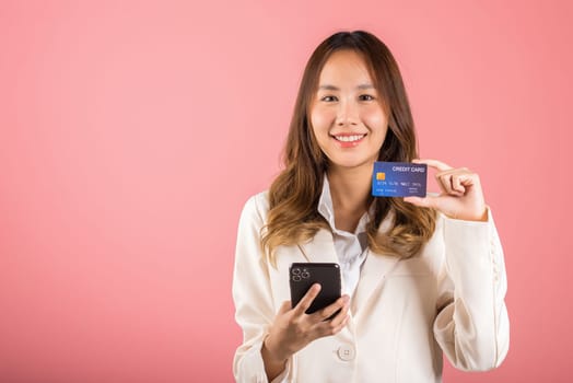 Happy Asian portrait beautiful cute young woman excited smiling hold mobile phone and plastic debit credit bank card, studio shot isolated on pink background, female using smartphone online shopping