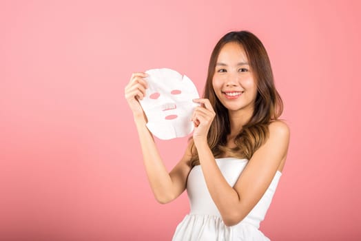Healthcare spa. Portrait beautiful female smiling holds facial sheet mask, Studio shot isolated on blue background, Asian woman holding purifying mask face on hands, Skin care healthcare cosmetic