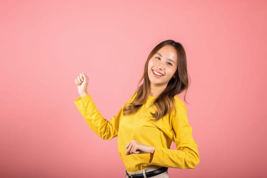 Asian young woman dancing with inspired face expression and raising hands up, Portrait of happy female model jocund in sneakers dancing, studio shot isolated on pink background, Time to relax