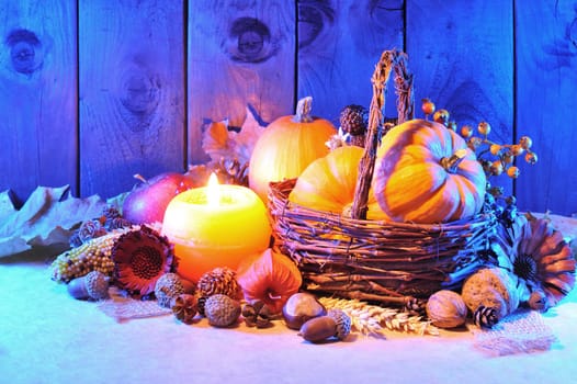 Thanksgiving – various pumpkins,nuts,corn and apple in a rattan basket with candlelight in blue evening light