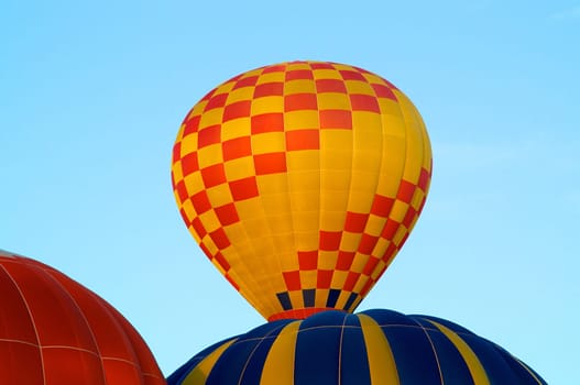 A red and yellow checkerboard colored hot air balloon is rising into the sky above a blue and yellow striped one.