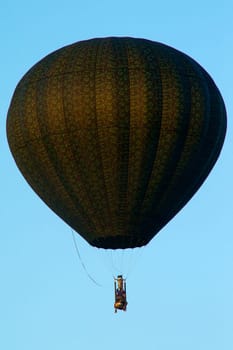 Looking up at a unique camouflaged hot air balloon floating in the clear blue sky.