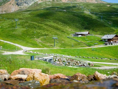 Landscape view of the Merano-2000 ski region with mountain inn in the background and green meadows and hiking trails as well as a water spring in the foreground in summer 2014