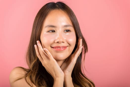 Eye skin treatment. Asian beautiful young woman smiling mask cosmetic patches gel under the eyes, Portrait female with natural makeup hydrogel eye patch on face, isolated on pink background, skincare
