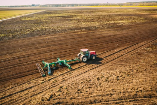 Aerial View. Tractor Plowing Field. Beginning Of Agricultural Spring Season. Cultivator Pulled By A Tractor In Countryside Rural Field Landscape.