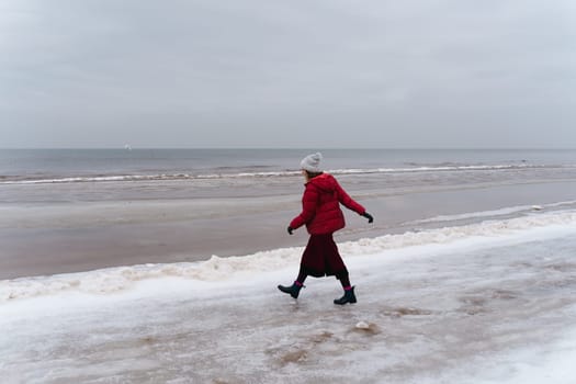 A woman in red walks in winter along the seashore.