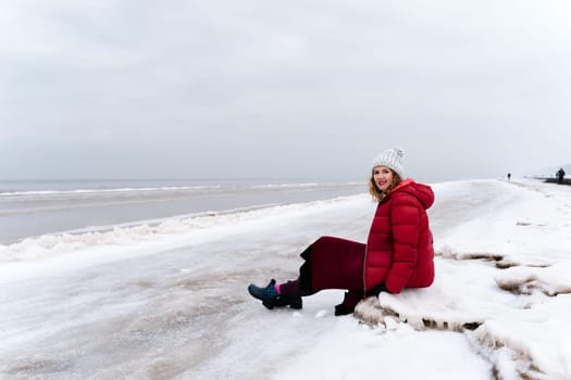A woman in warm winter clothes rests sitting on the beach.
