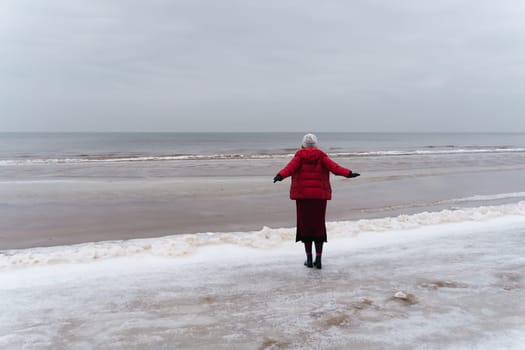 A woman stands looking at the sea spreading her arms to the sides, the view from behind.