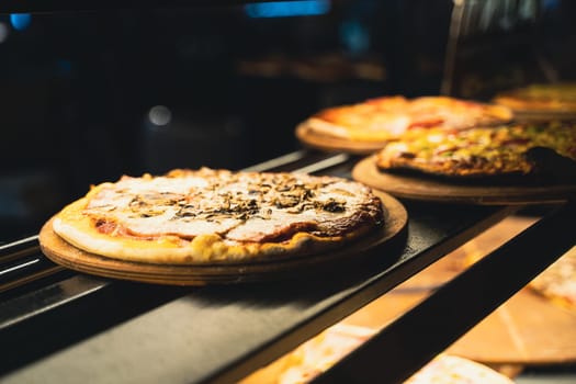 perspective view closeup of different kinds of pizza on wooden plates on the shelves of street food shop window