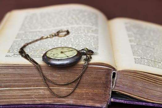 An antique pocket watch leans against an old book with yellowed pages