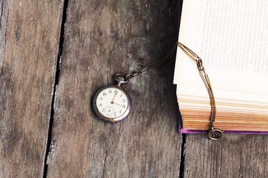 An antique pocket watch and an old book on an old wooden table